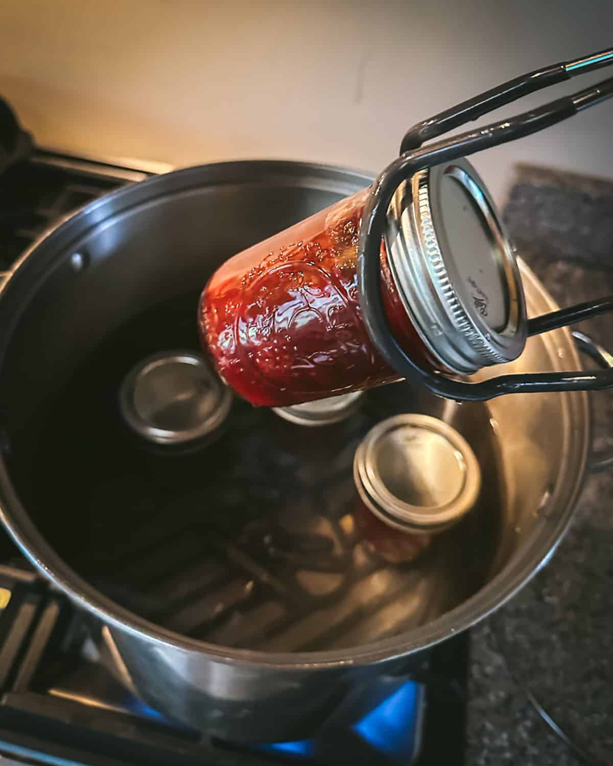 A jar lifter placing jars of cranberry sauce into a water bath canner. 