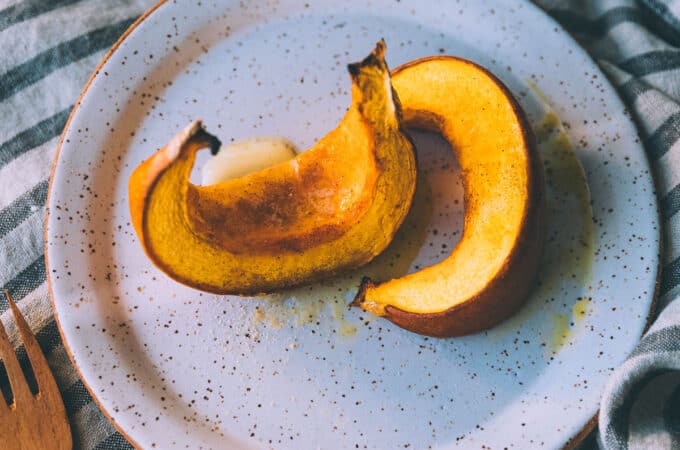 A white plate with 2 roasted pumpkin wedges on it, sitting on a gray and white towel.