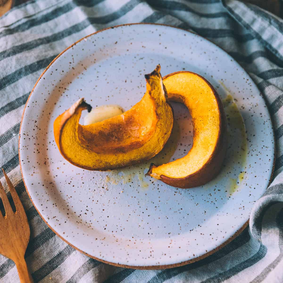 A white plate with 2 roasted pumpkin wedges on it, sitting on a gray and white towel. 