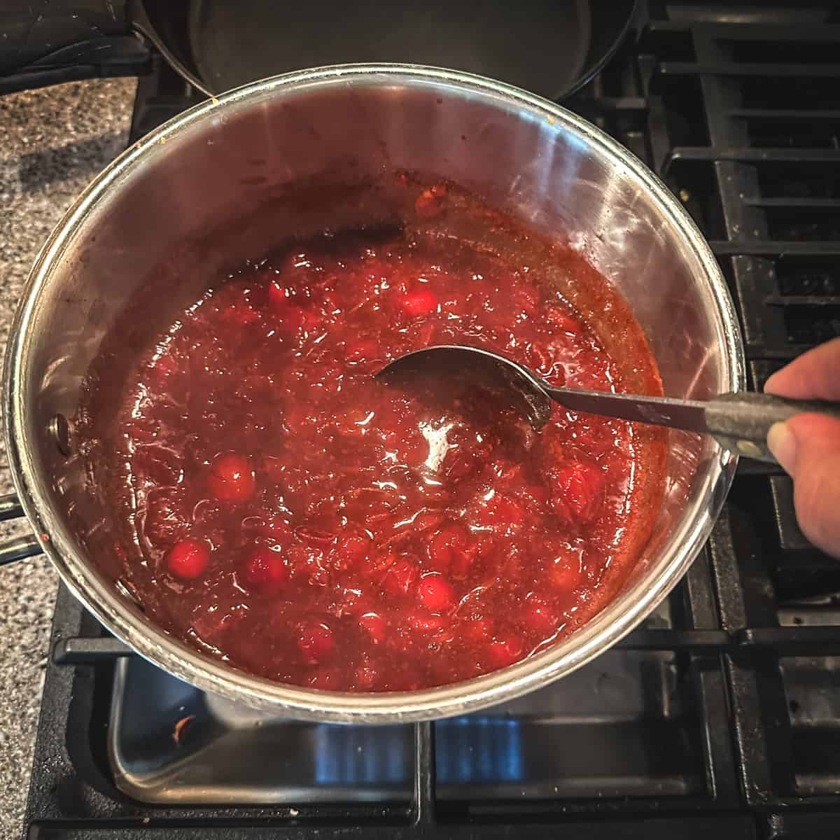 Cranberry sauce on the stove being stirred with a spoon, top view. 