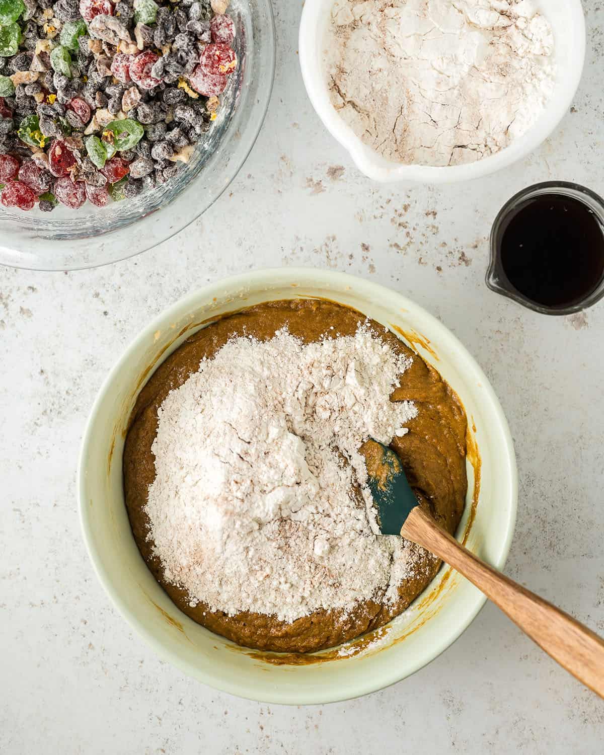 A white mixing bowl with dry cake ingredients in it being mixed with a wooden spoon, top view.