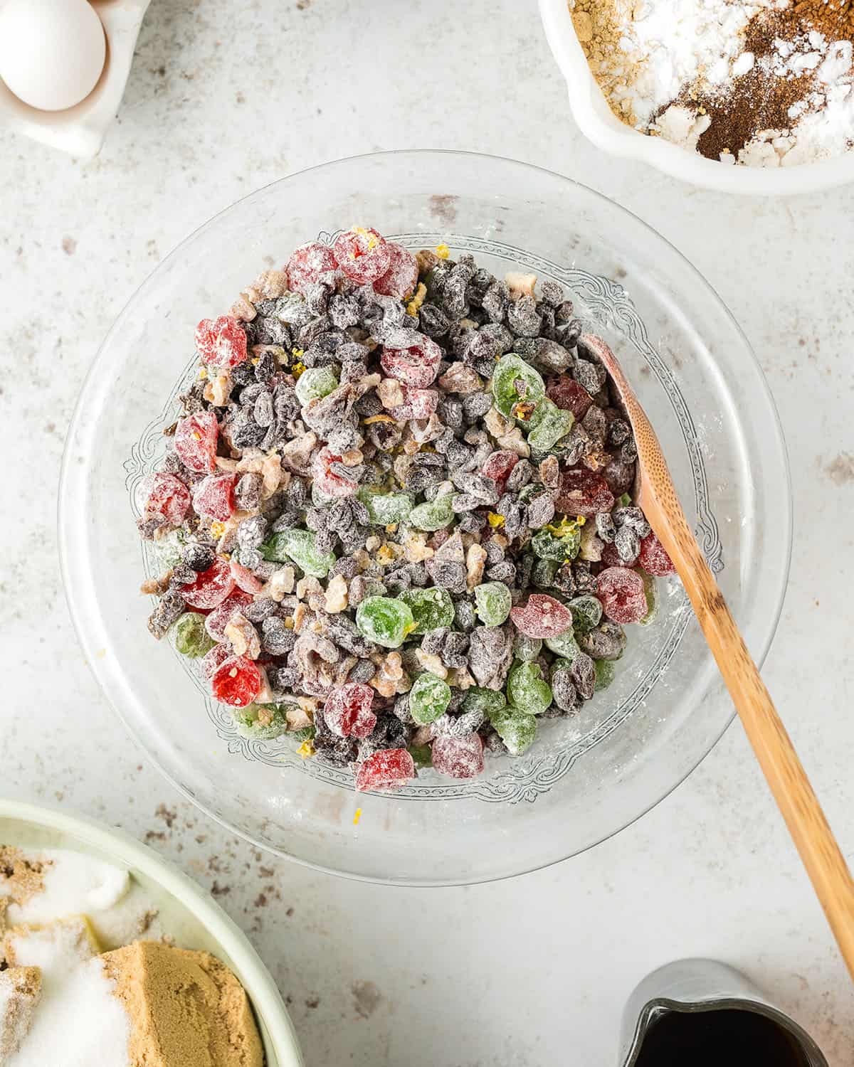 A bowl of dried and candied fruit coated with flour in a mixing bowl with a wooden spoon. 