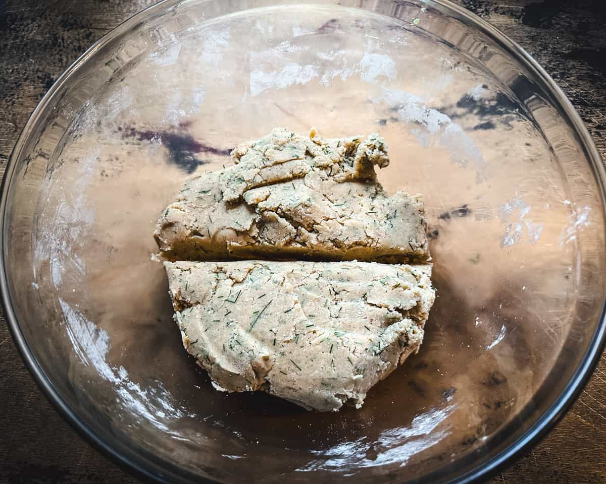 A clear bowl with pine needle cookie dough cut in half, on a dark wood surface, top view. 