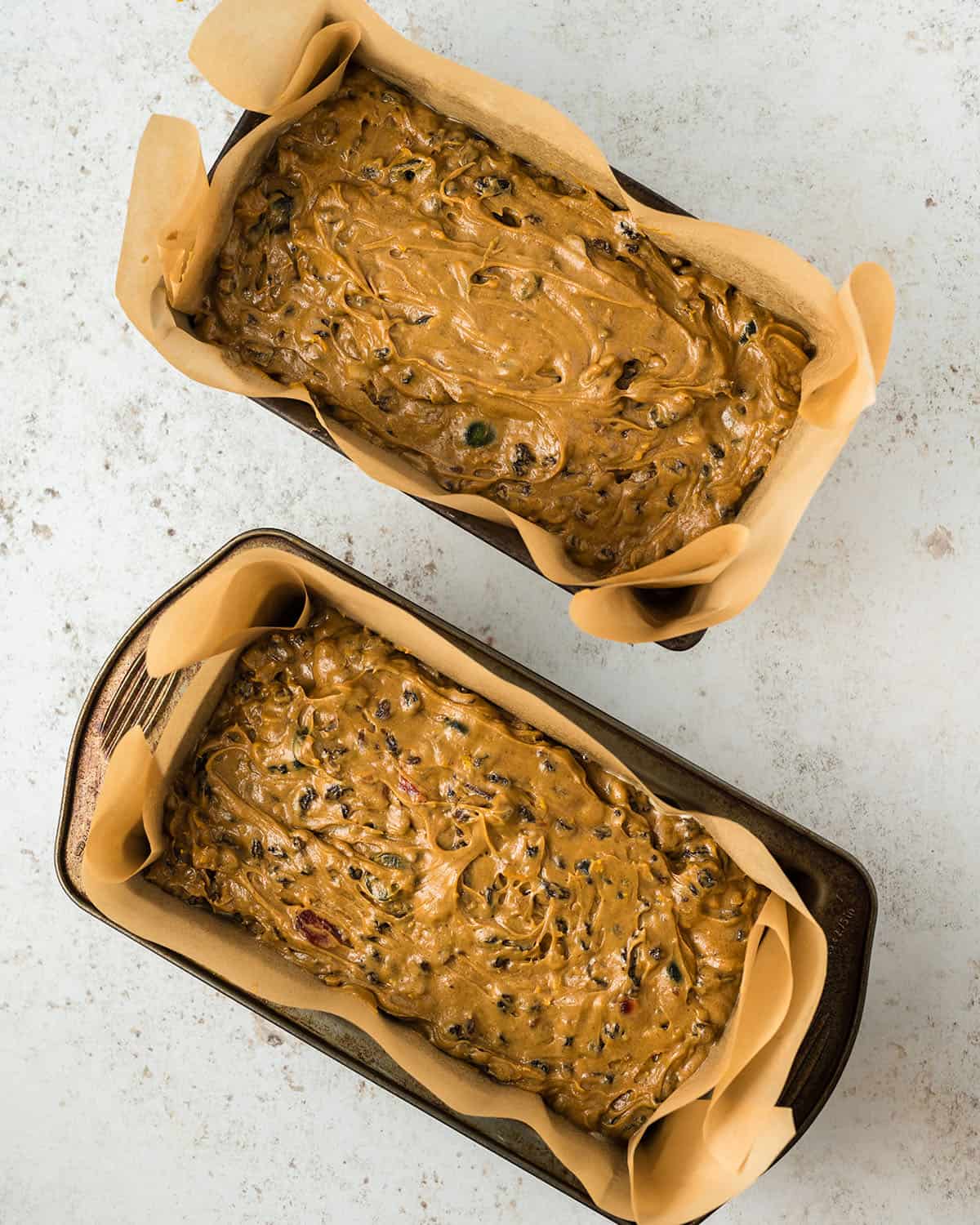 2 loaf pans with fruit cake batter in them, top view. 