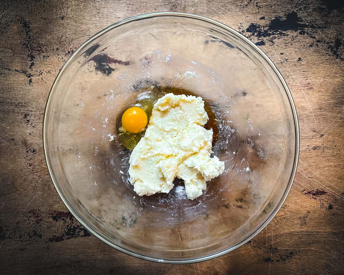 Creamed butter and sugar and an egg in a clear bowl, on a wood surface. 