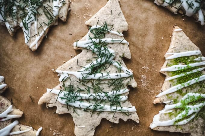 Tree shaped sugar cookies with pine needles and icing on top, on a wood surface.
