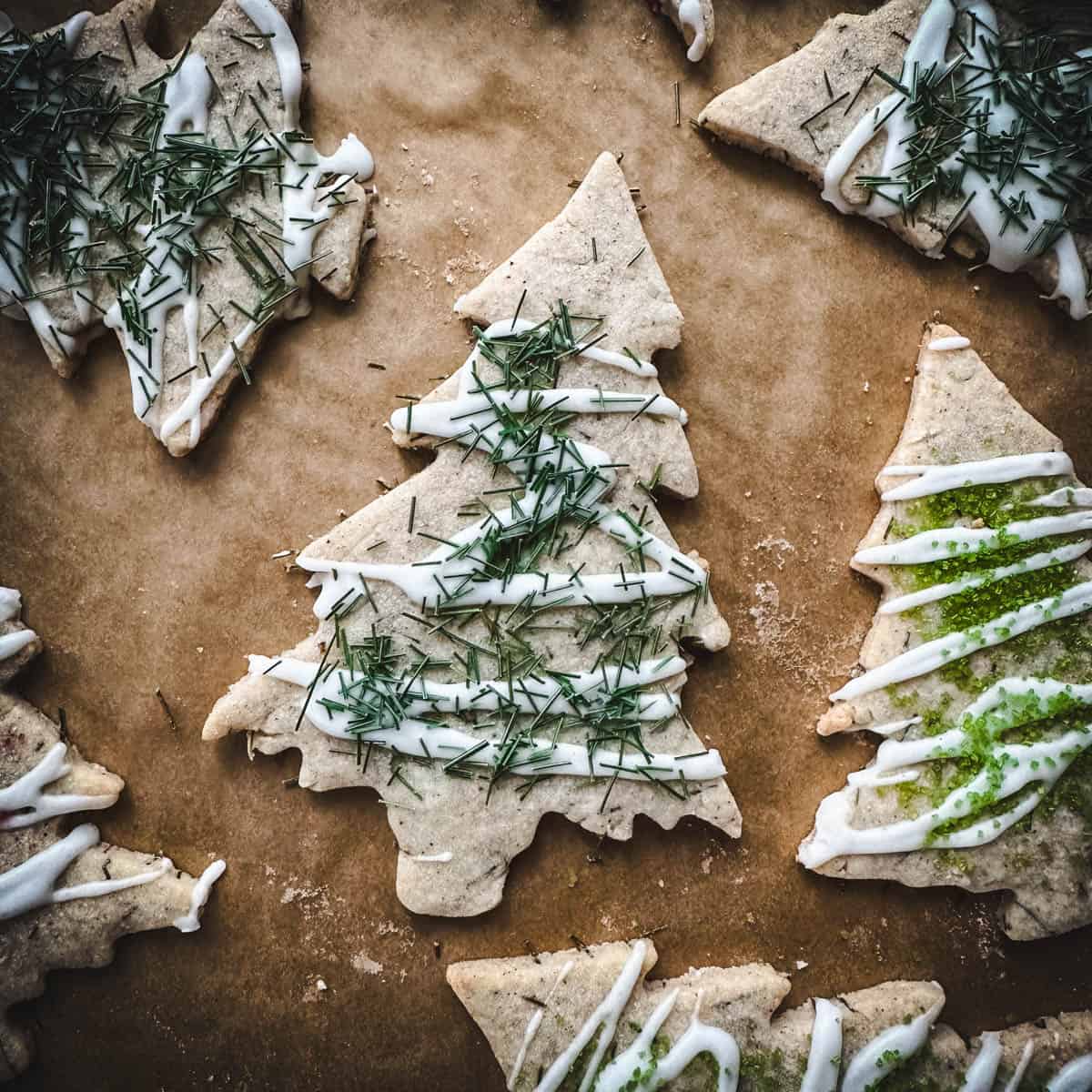 Tree shaped sugar cookies with pine needles and icing on top, on a wood surface.