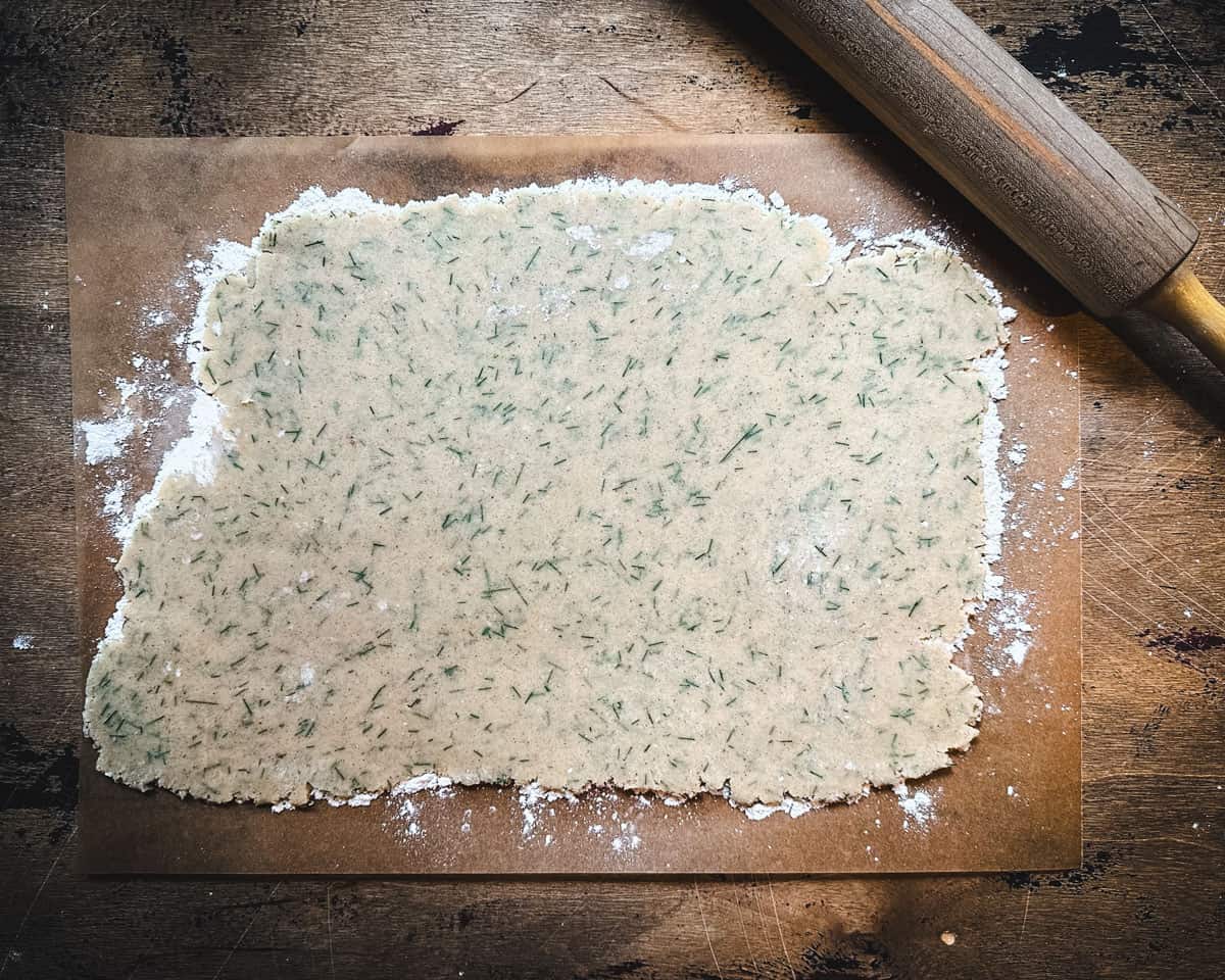Pine needle sugar cookie dough rolled out on parchment paper on a wood surface, with a rolling pin in the corner.
