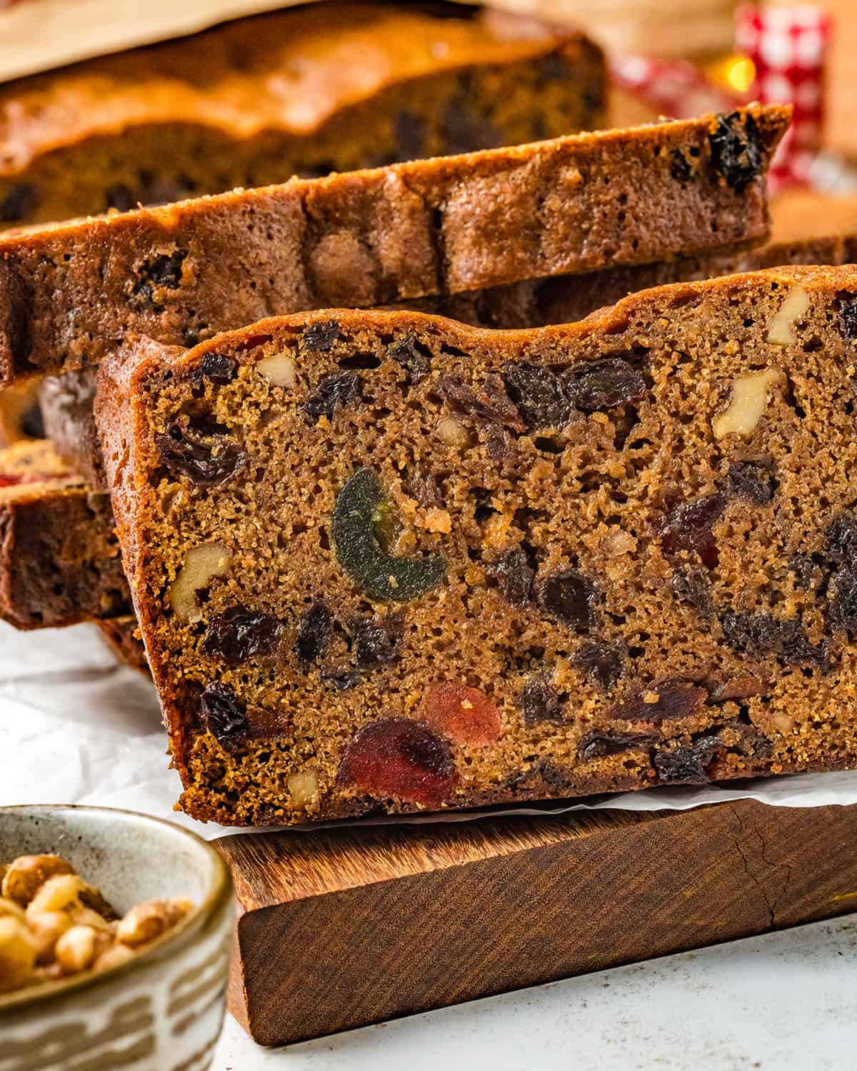 Slices of fruit cake face up on white parchment paper, side view.