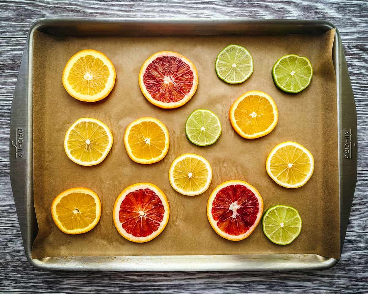 A baking sheet lined with parchment paper, with a mix of citrus slices in one layer on the pan.