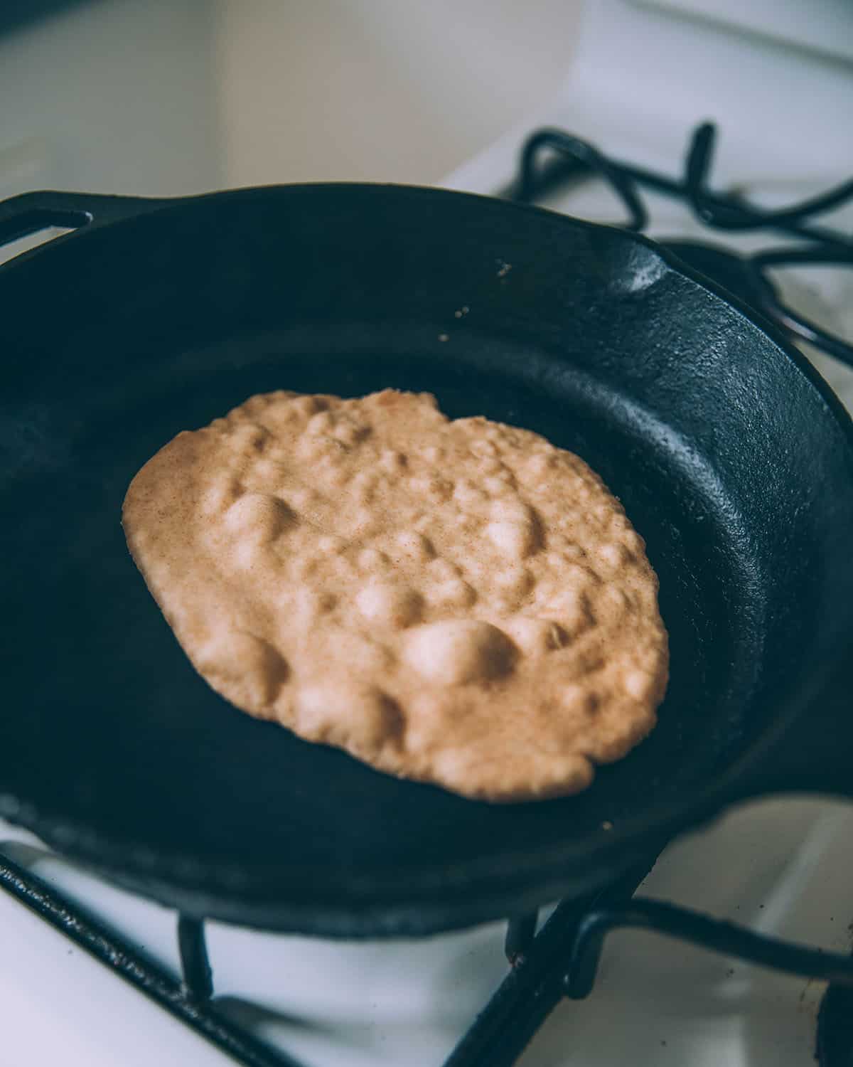 A sourdough flatbread cooking in a cast iron skillet, it is bubbling on the top. 