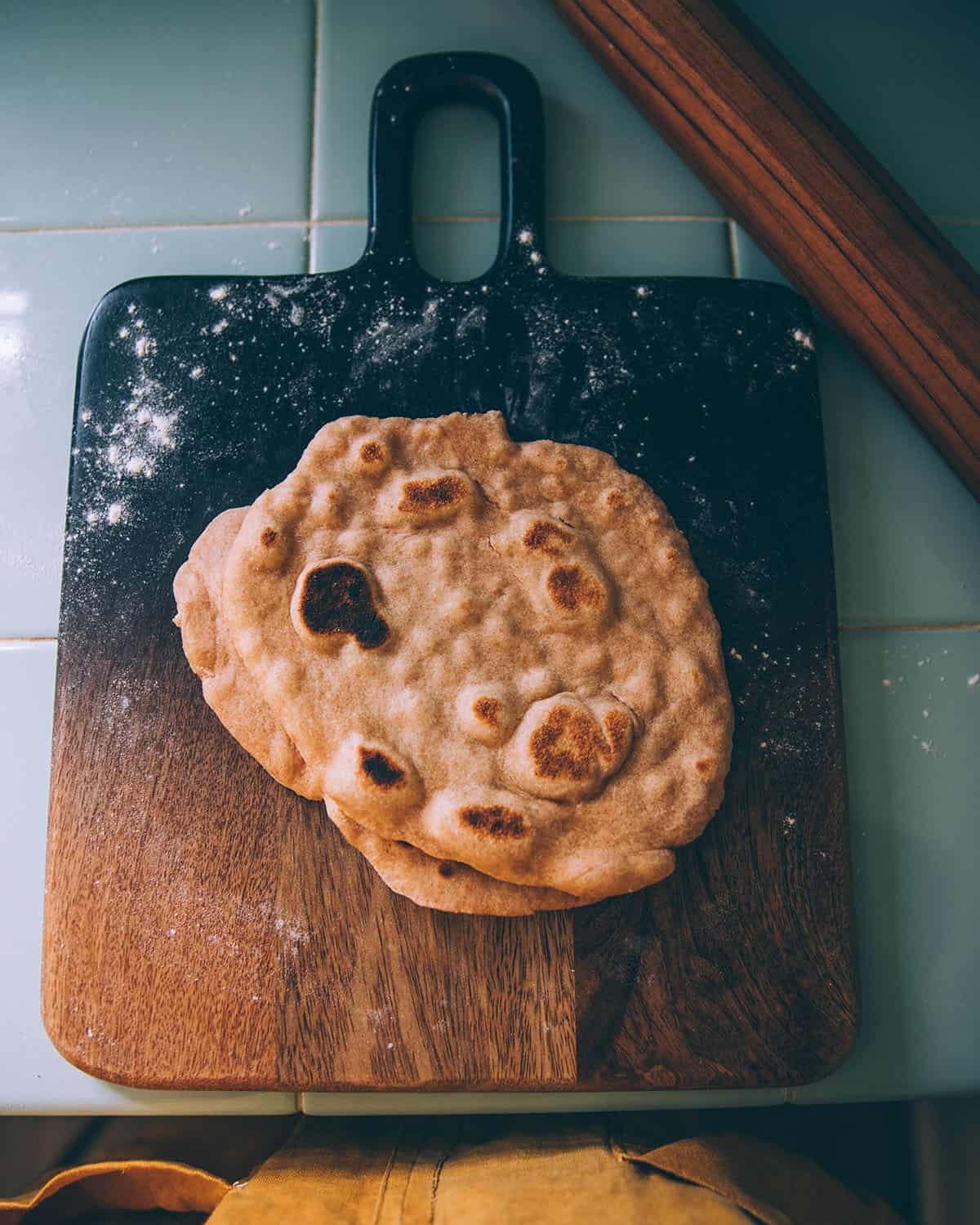 A dark wood cutting board with a cooked flatbread on it. 