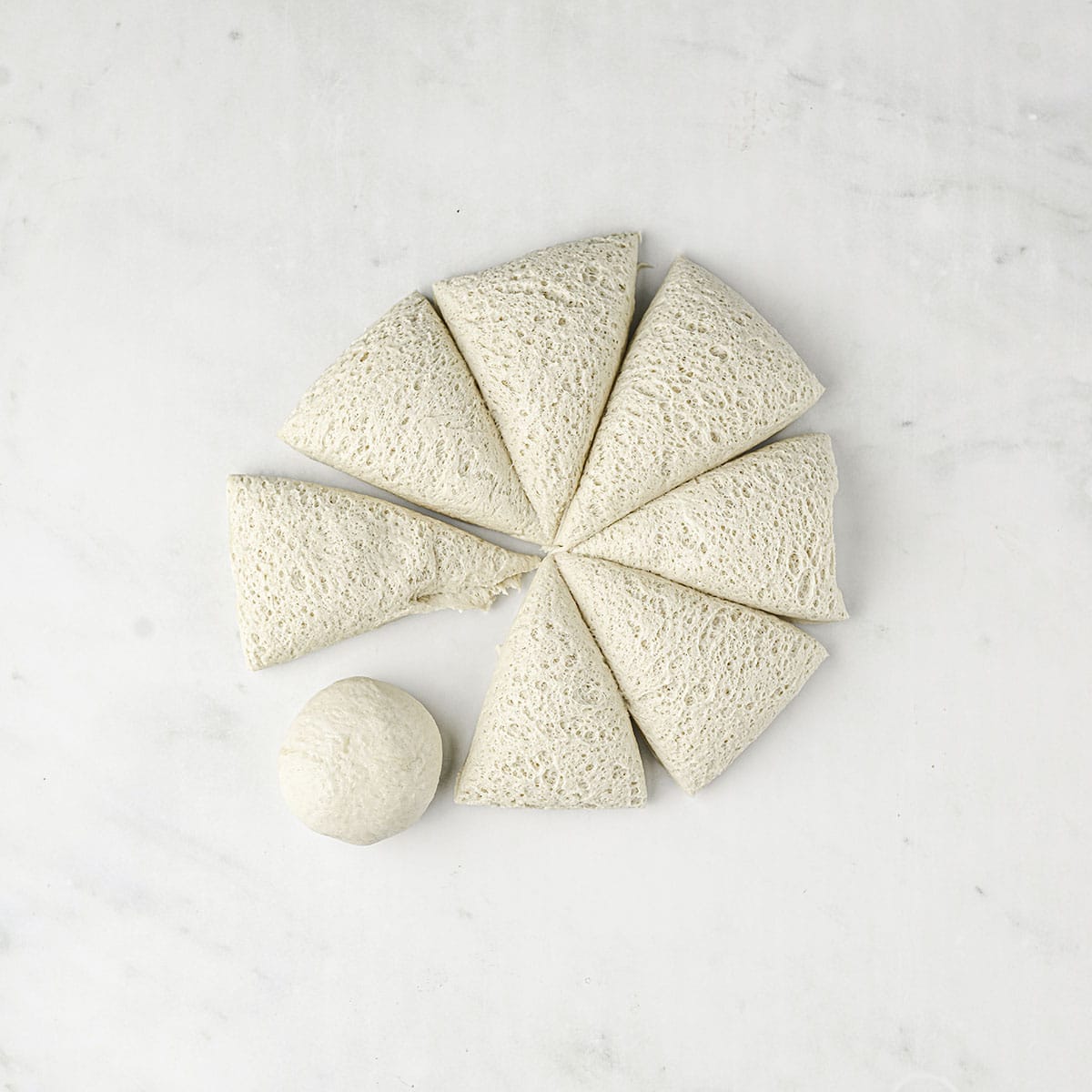 Dough on a white surface, cut into 8 triangular pieces, with one rolled into a ball.