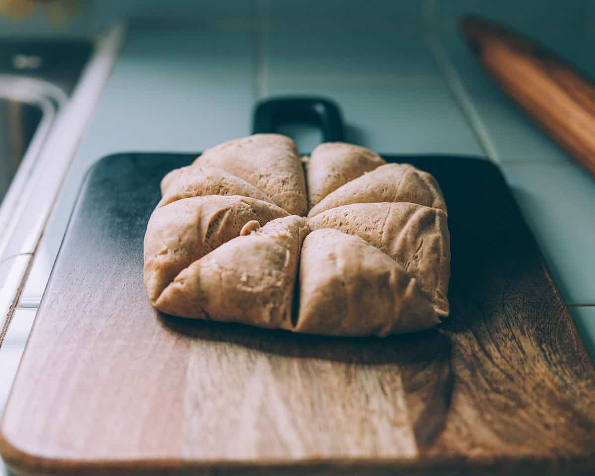 A dark wood cutting board with a dough ball cut into 8 triangle pieces like a pie.