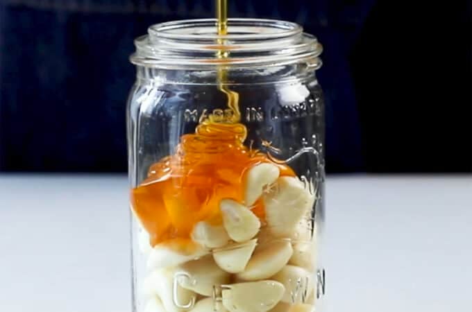 A jar of garlic with honey pouring over it.