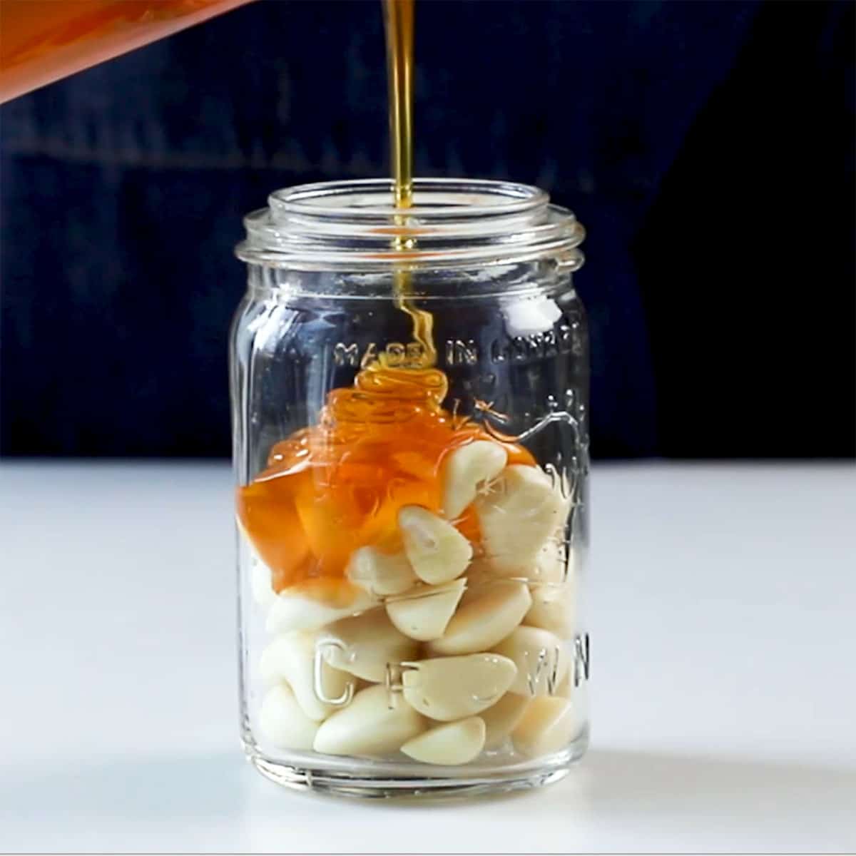 A jar of garlic with honey pouring over it. 