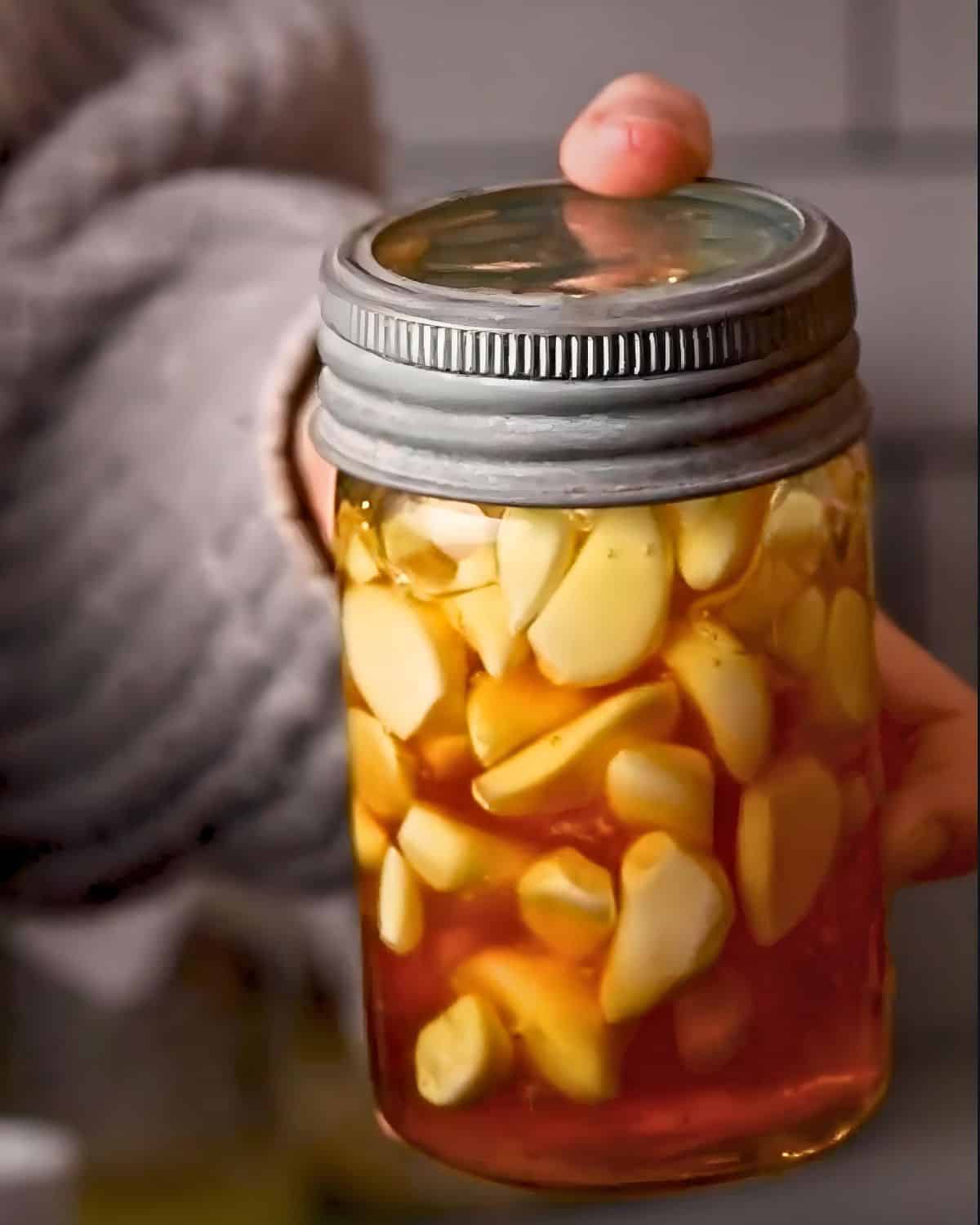 a hand holding a jar of fermented honey garlic