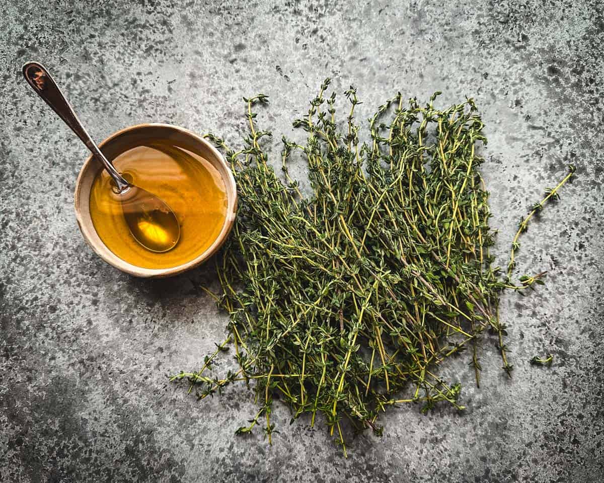 Fresh thyme sprigs on a gray countertop with a small bowl of honey with a spoon in it. 