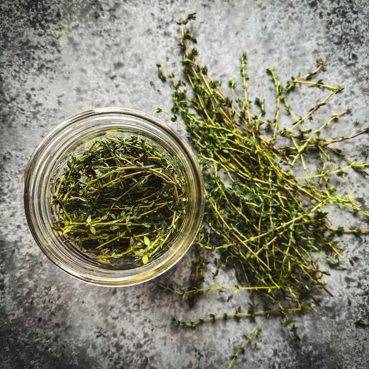 Fresh thyme sprigs in a mason jar, top view, surrounded by more fresh thyme. 