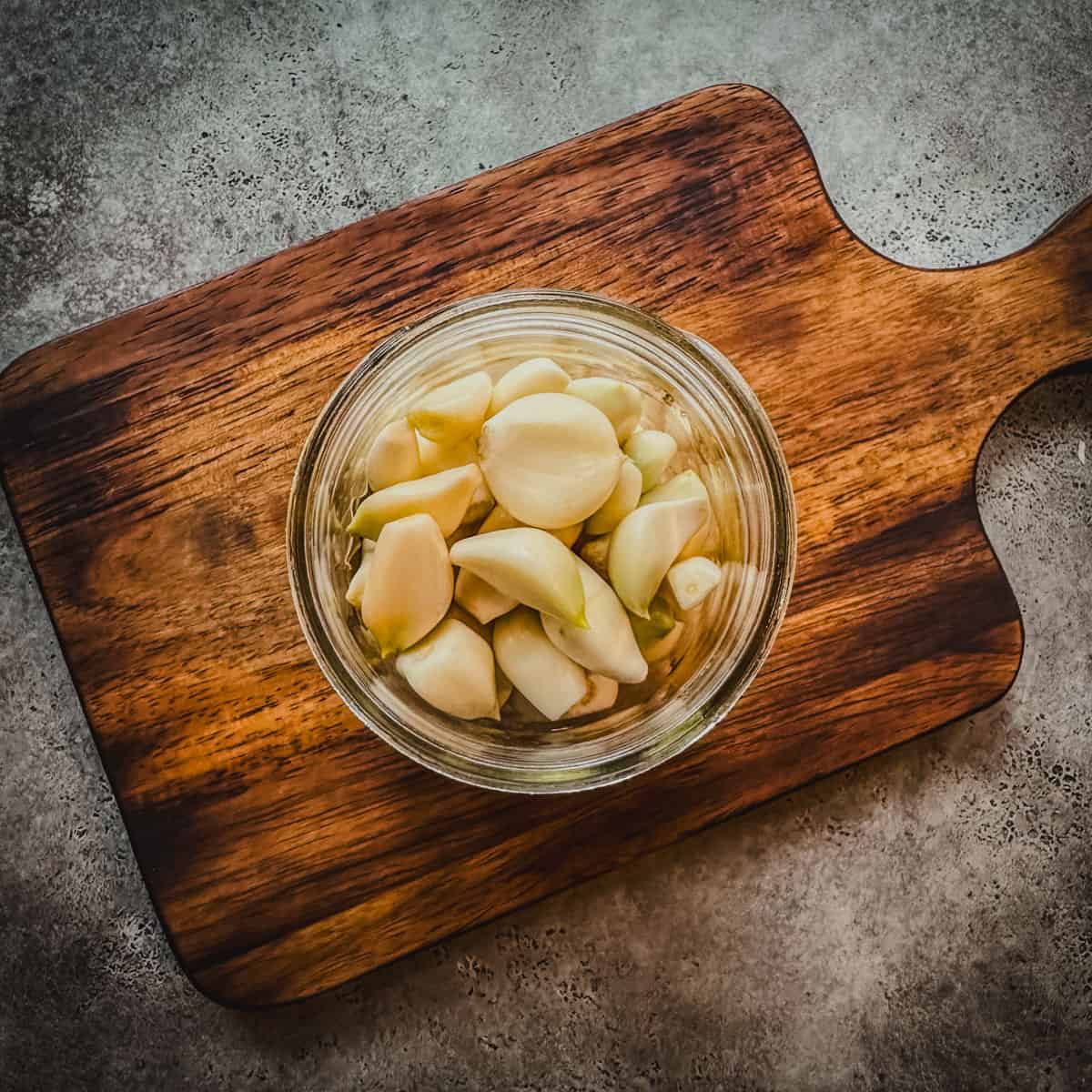 Peeled garlic cloves in a pint jar on a wood cutting board, top view.