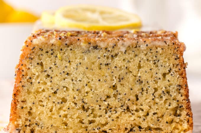 A lemon poppy seed cake showing the cut side so the poppy seeds and yellow of the lemon cake show, with lemon slices on top.