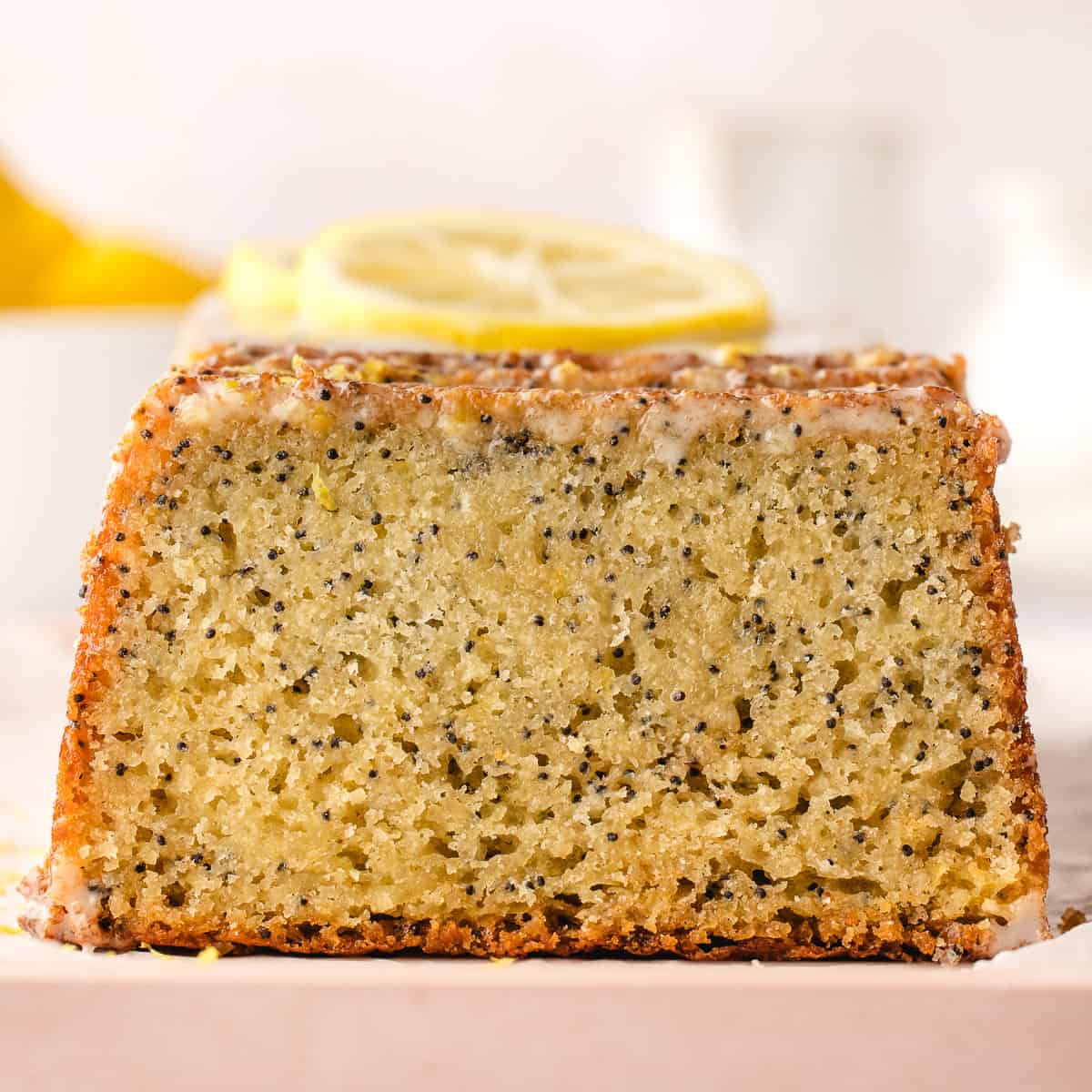 A lemon poppy seed cake showing the cut side so the poppy seeds and yellow of the lemon cake show, with lemon slices on top. 