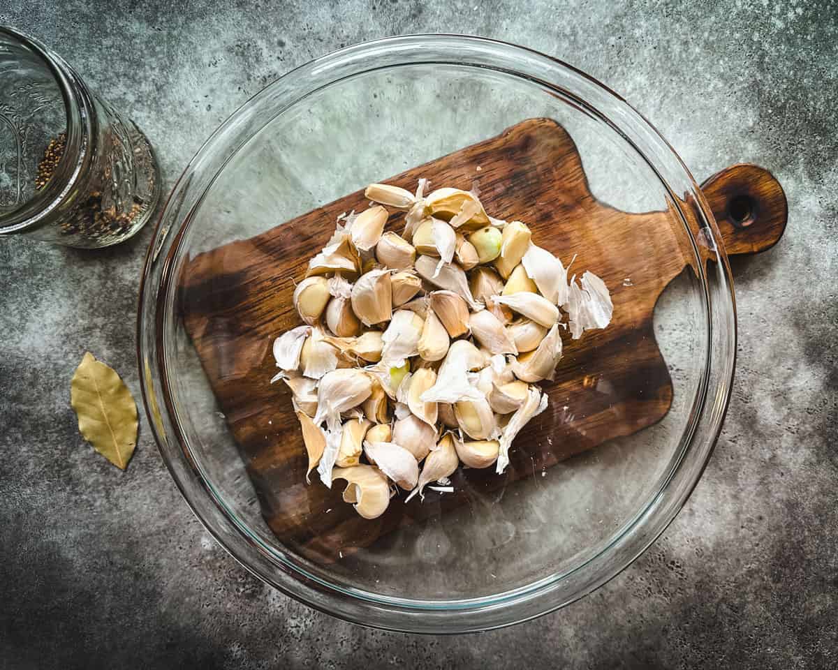 A bowl of garlic cloves for peeling, on a wood cutting board with a gray background, top view. 