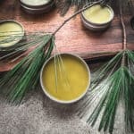 Pine salve in tins, on a wood cutting board surrounded by pine fronds.