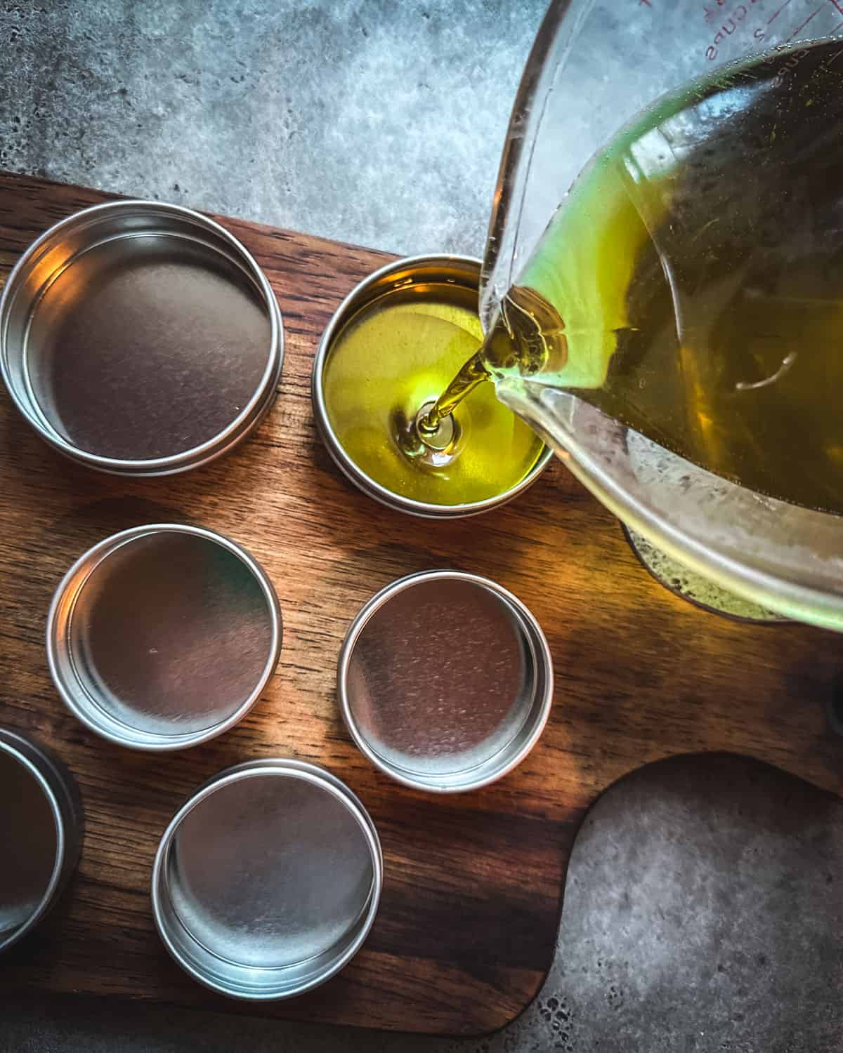 Pine salve melted and pouring into tins sitting on a wood cutting board. 