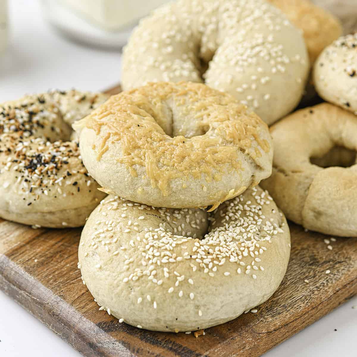 Sourdough bagels topped with sesame seeds, cheese, and everything bagel seasoning on a wood cutting board with a white counter background. 