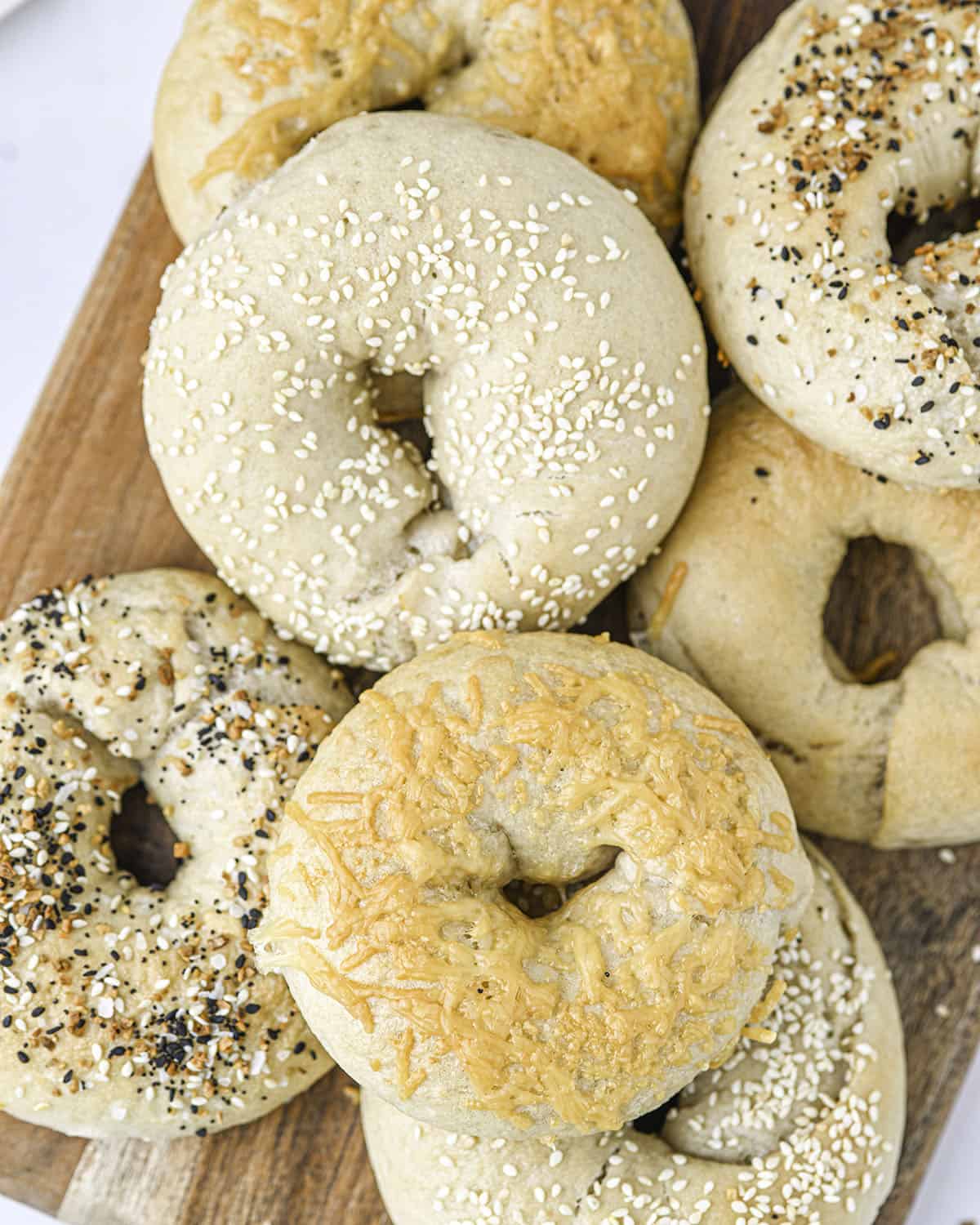 Sourdough bagels topped with sesame seeds, crispy cheese, and everything bagel seasoning on a wood cutting board on a white counter, top view.