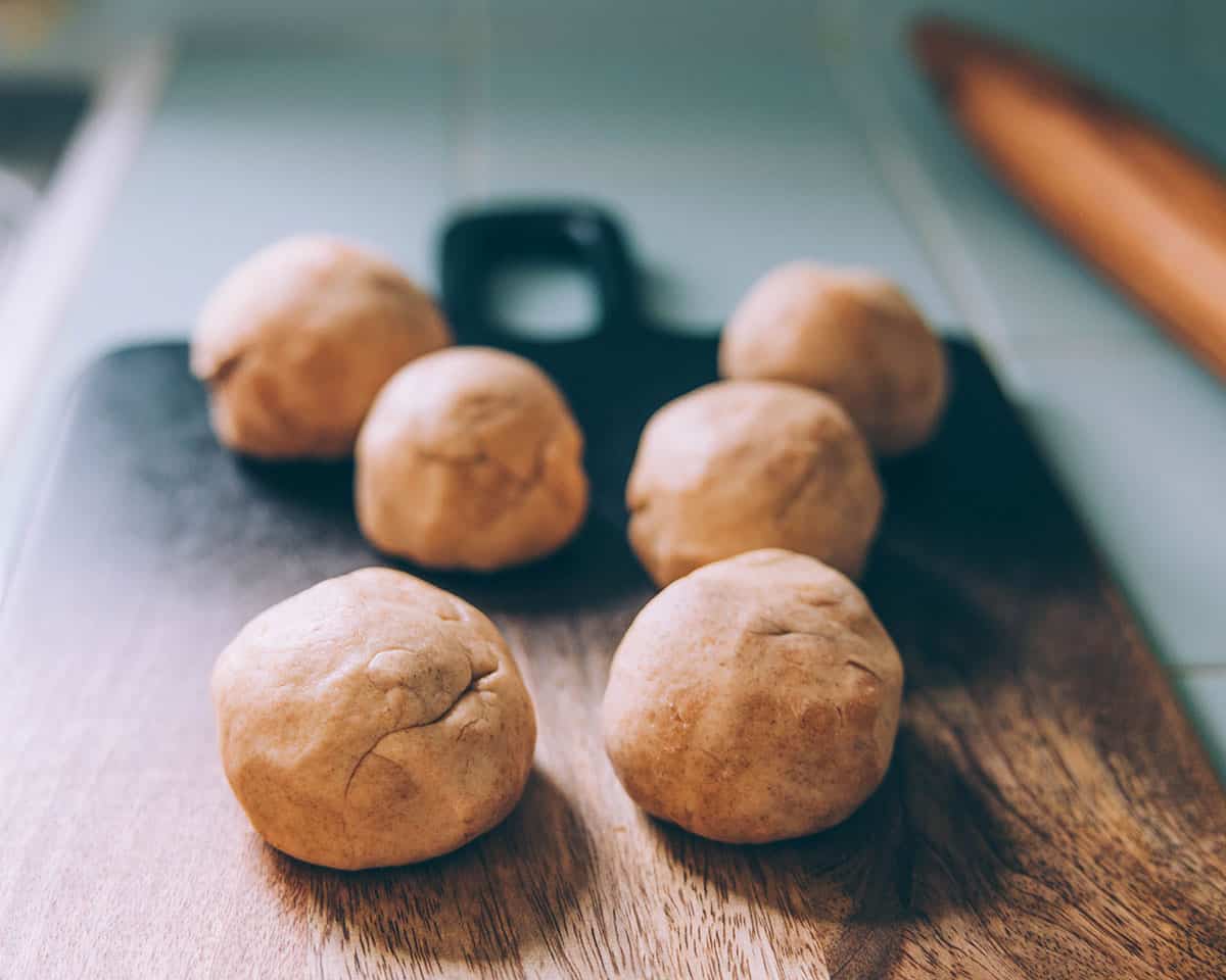 6 small balls of dough on a dark wood cutting board in natural light. 