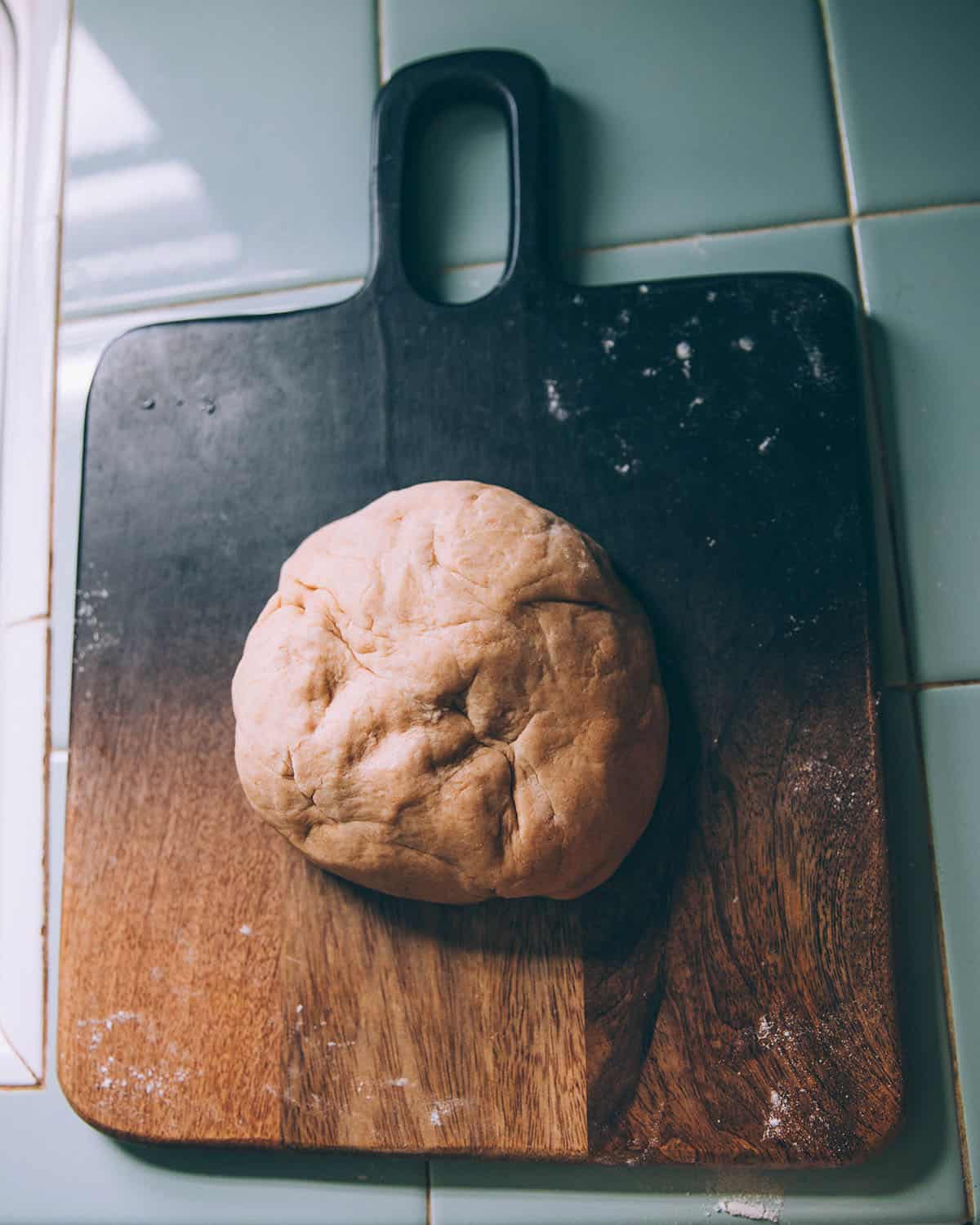 A dark wood cutting board with a ball of dough on it. 