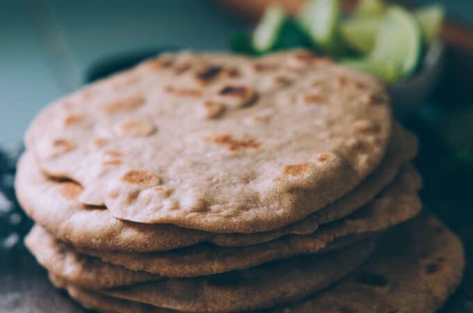 A stack of whole wheat sourdough flatbreads on a wood surface with limes in the background.