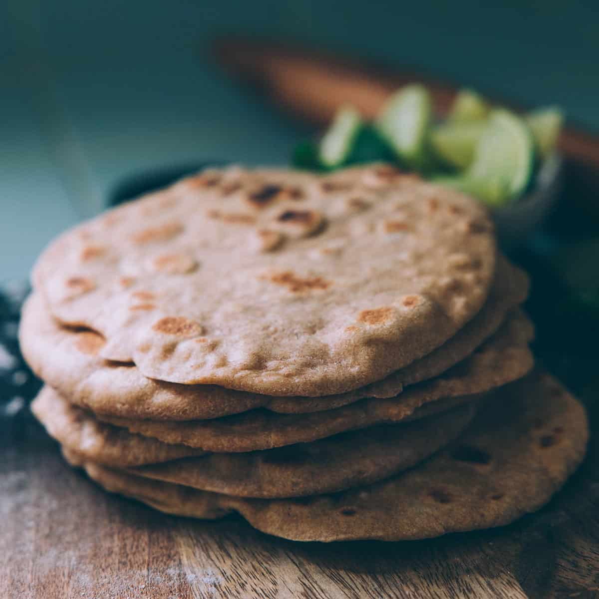 A stack of whole wheat sourdough flatbreads on a wood surface with limes in the background. 