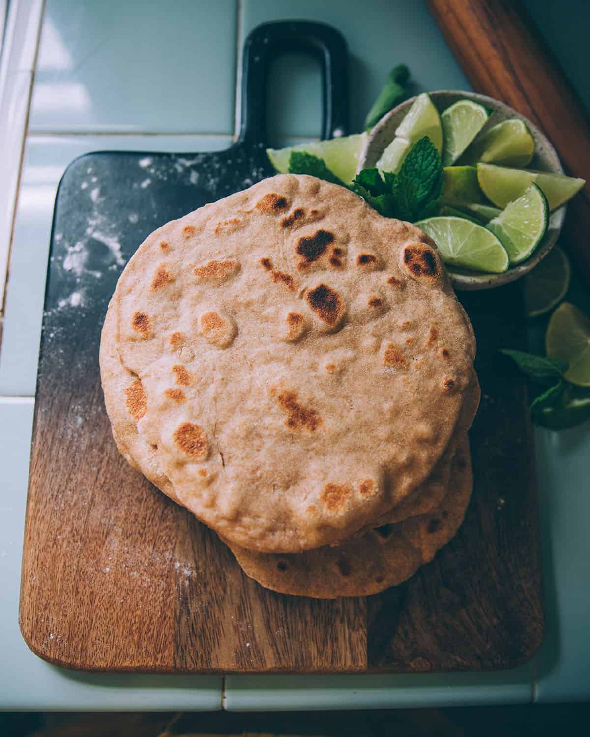 A stack of sourdough flatbreads on a dark wood cutting board.