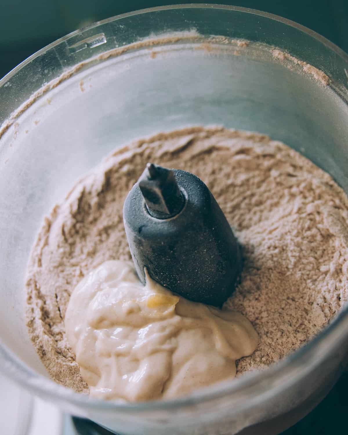 A food processor with dry ingredients and topped with sourdough starter. 
