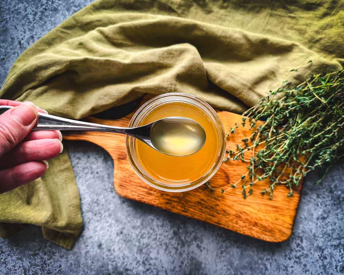 A spoon lifting out of a jar with thyme cough syrup in it, top view. 