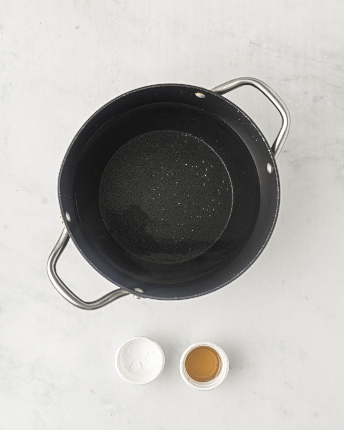 A pot of water with small white bowls next to it filled with baking soda and honey. Top view. 