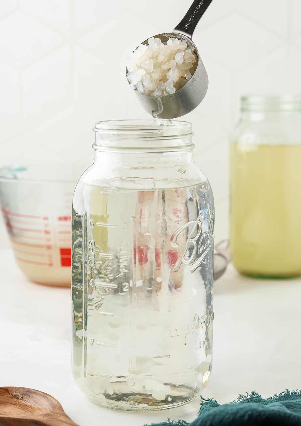 Kefir grains pouring from a cup into a jar of water. 