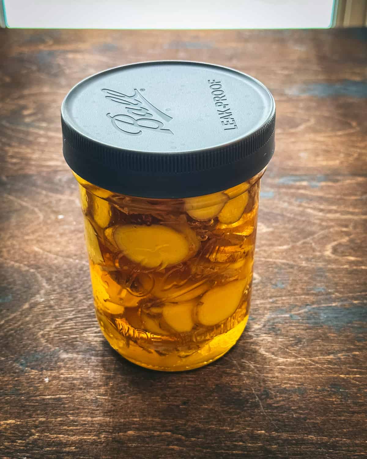 A jar of fermenting ginger in honey with a lid on a dark wood surface. 