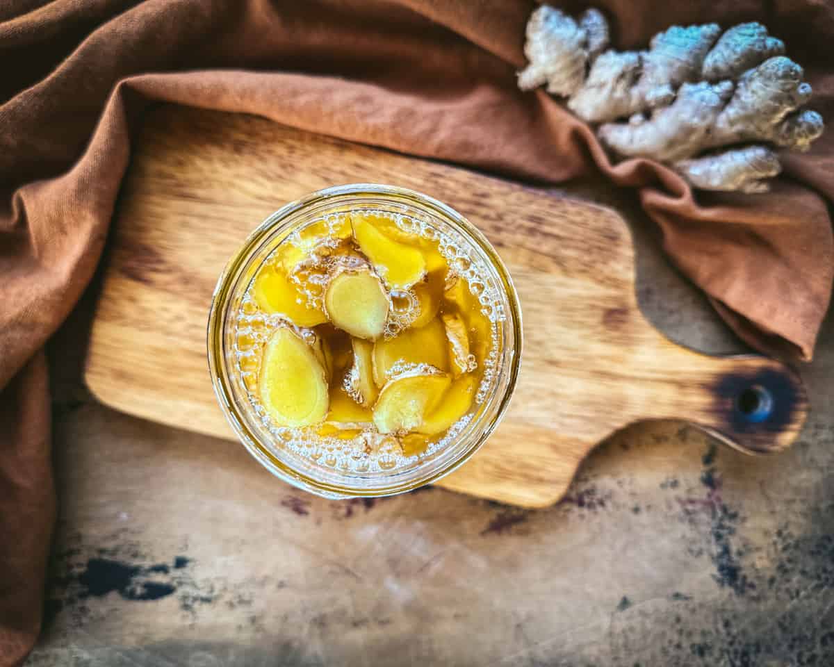 Ginger honey with bubbles on top on a wood cutting board, surrounded by rust cloth and ginger root, top view. 