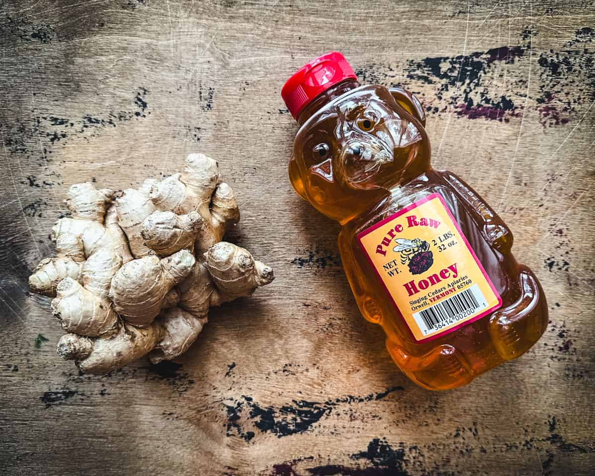 A honey bear looking cute and fresh ginger root on a wood surface. 