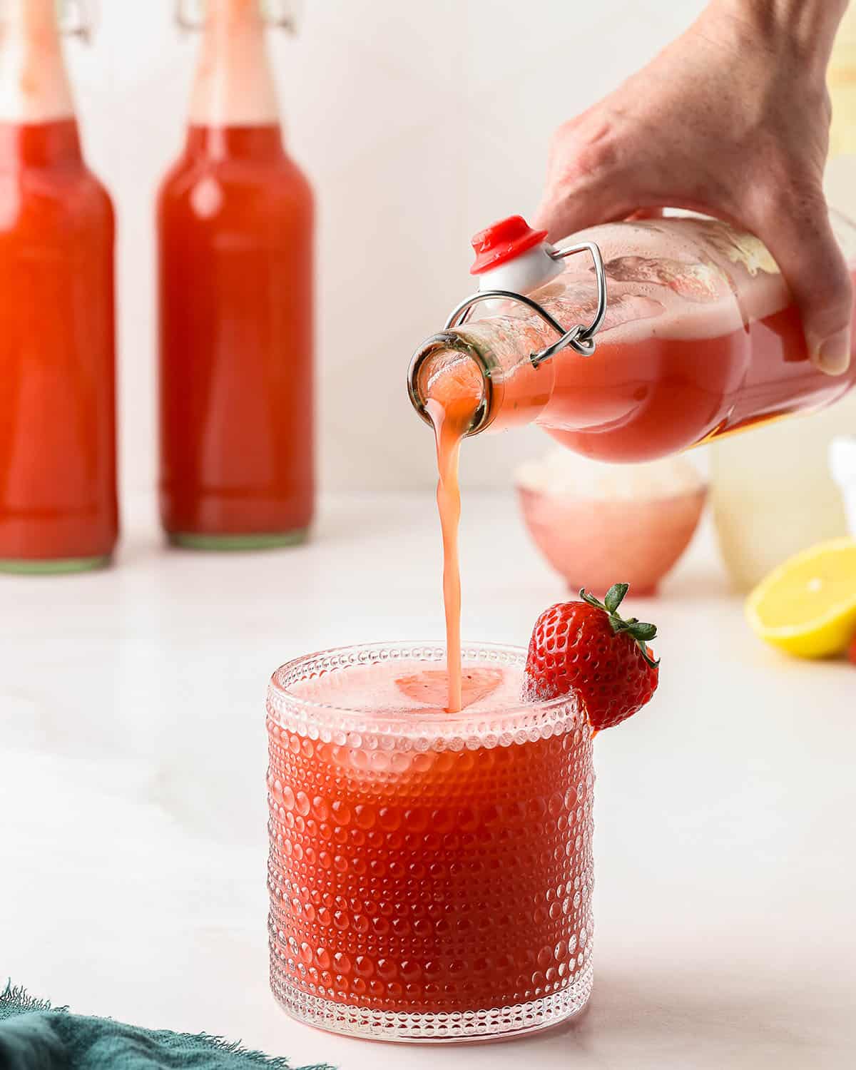 A bottle of strawberry water kefir pouring into a glass. 