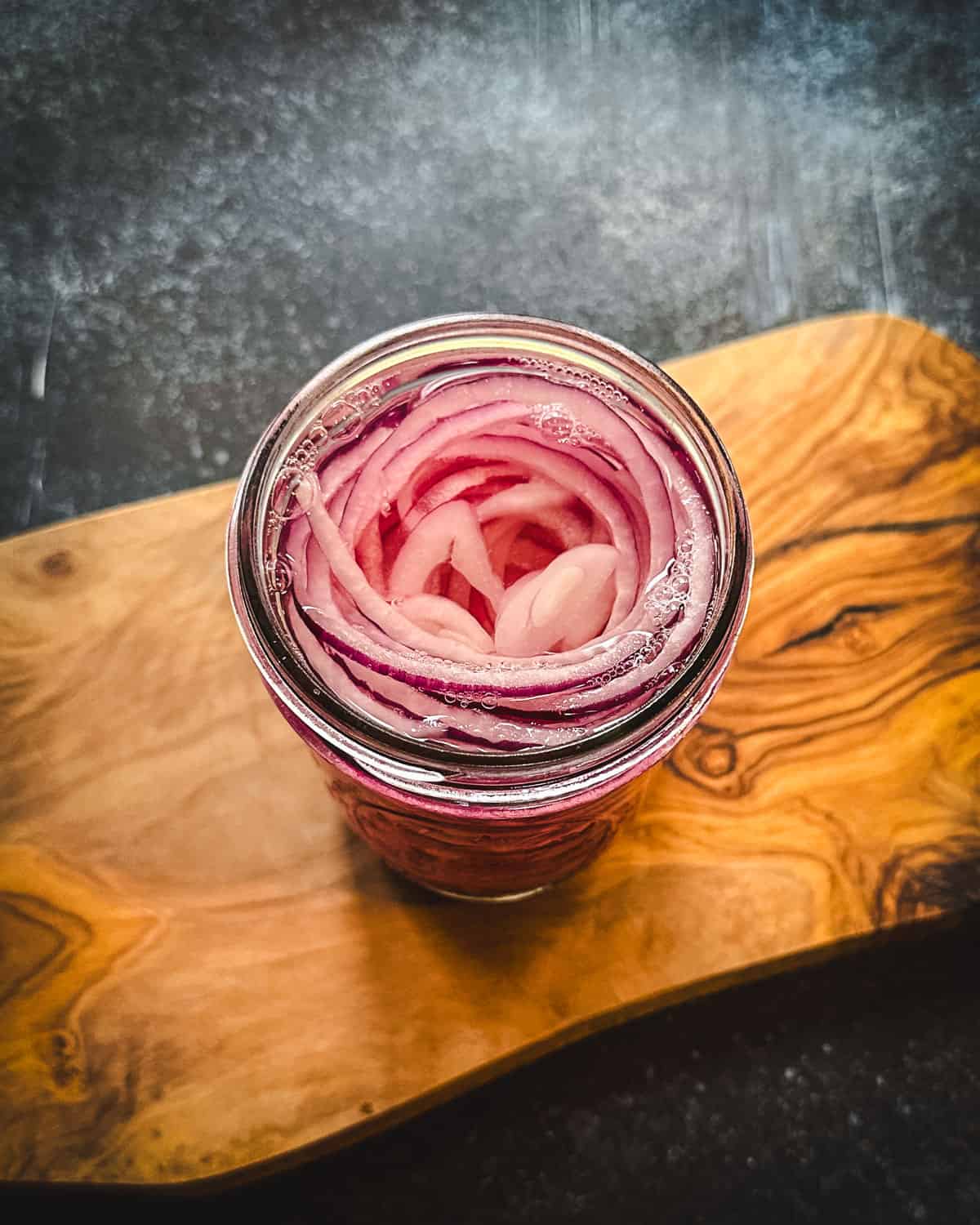 Red onions in vinegar brine in a jar on a wood cutting board, top view. 