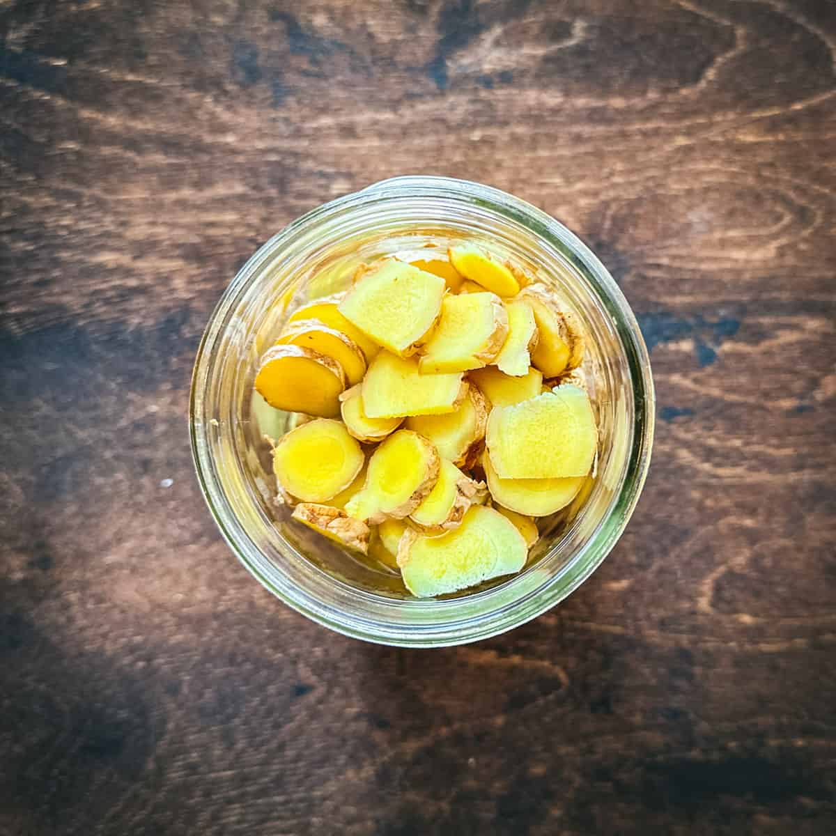 Sliced ginger in a mason jar on a dark wood surface, top view. 