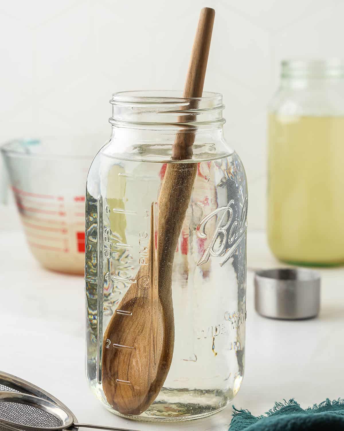 A wooden spoon stirring sugar into a jar of water.