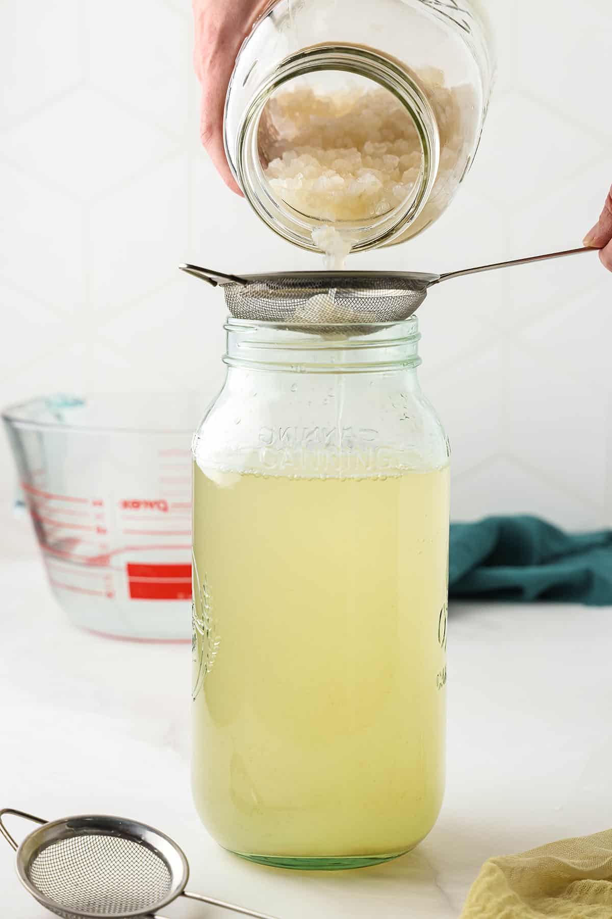 A jar with a small strainer on top with fermented water kefir being poured in, reserving the kefir grains. 