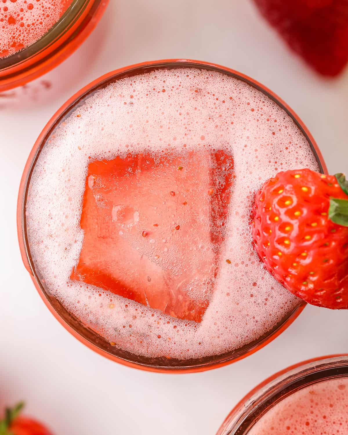Strawberry water kefir in a jar with an ice cube and fizz foaming the top, garnished with a fresh strawberry. Top view. 