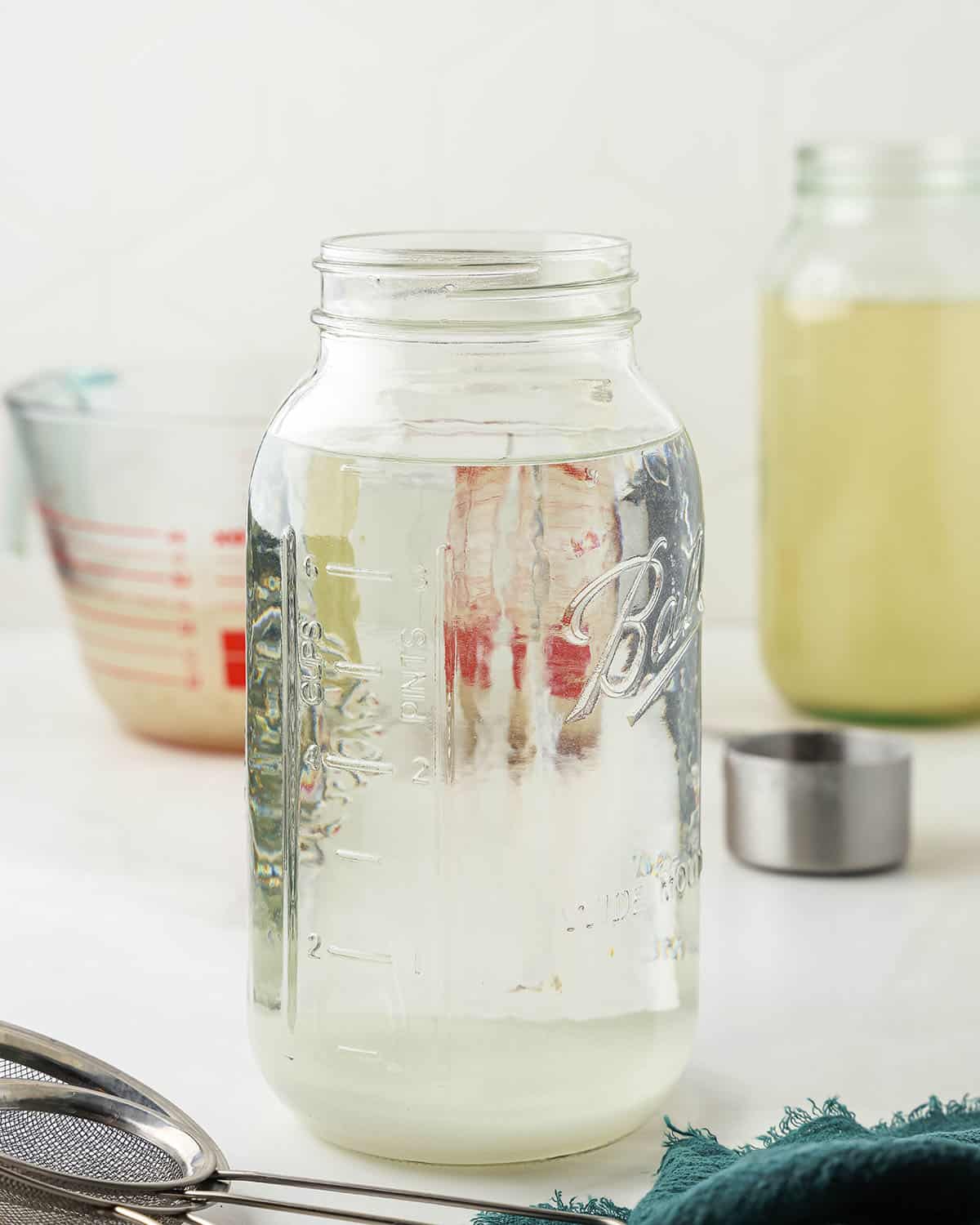 Mason jar full of water with room at the top, and other water kefir ingredients in the background. 